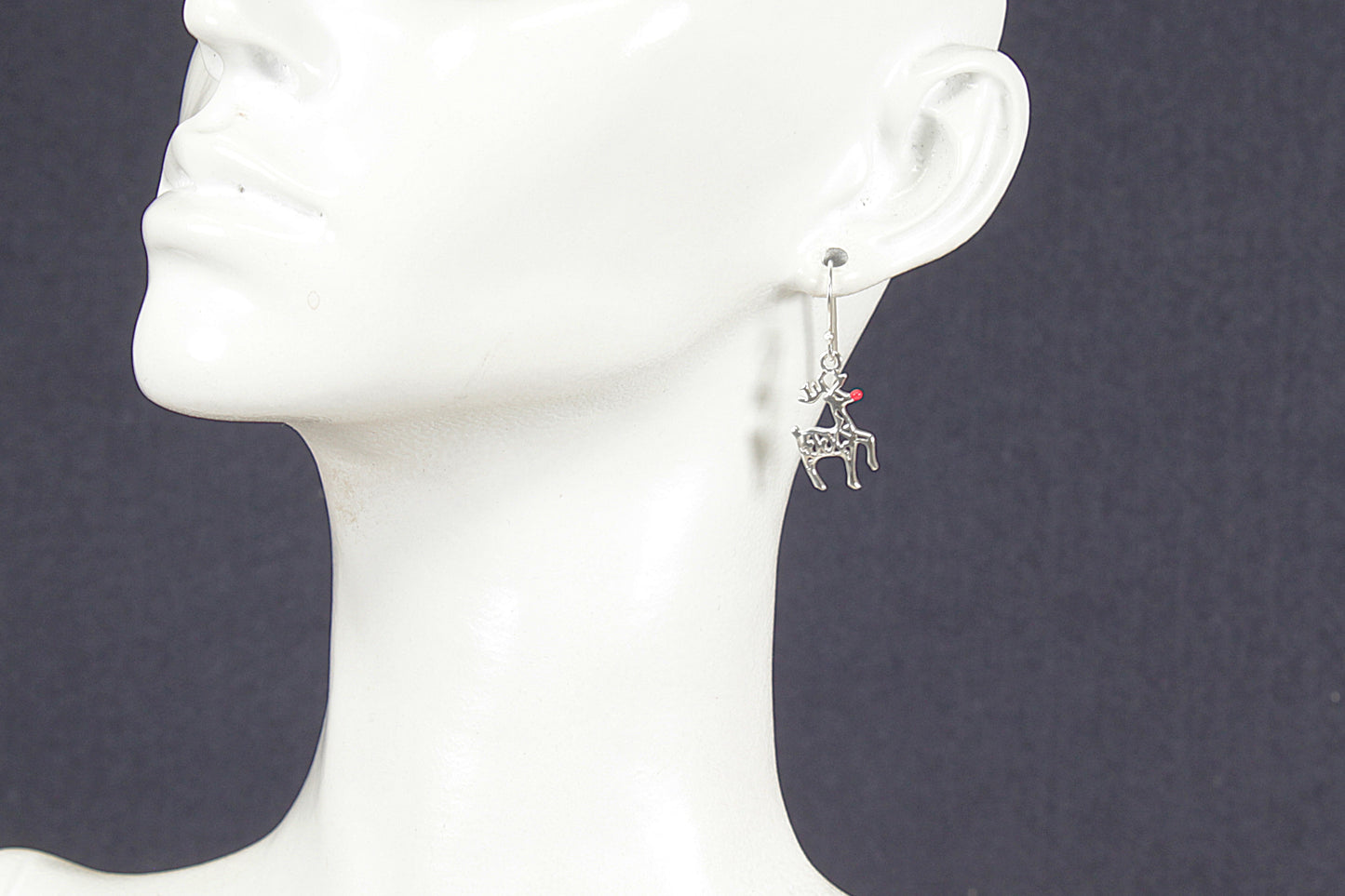 Silver earring with a small Rudolph charm on a white mannequin head against a dark background