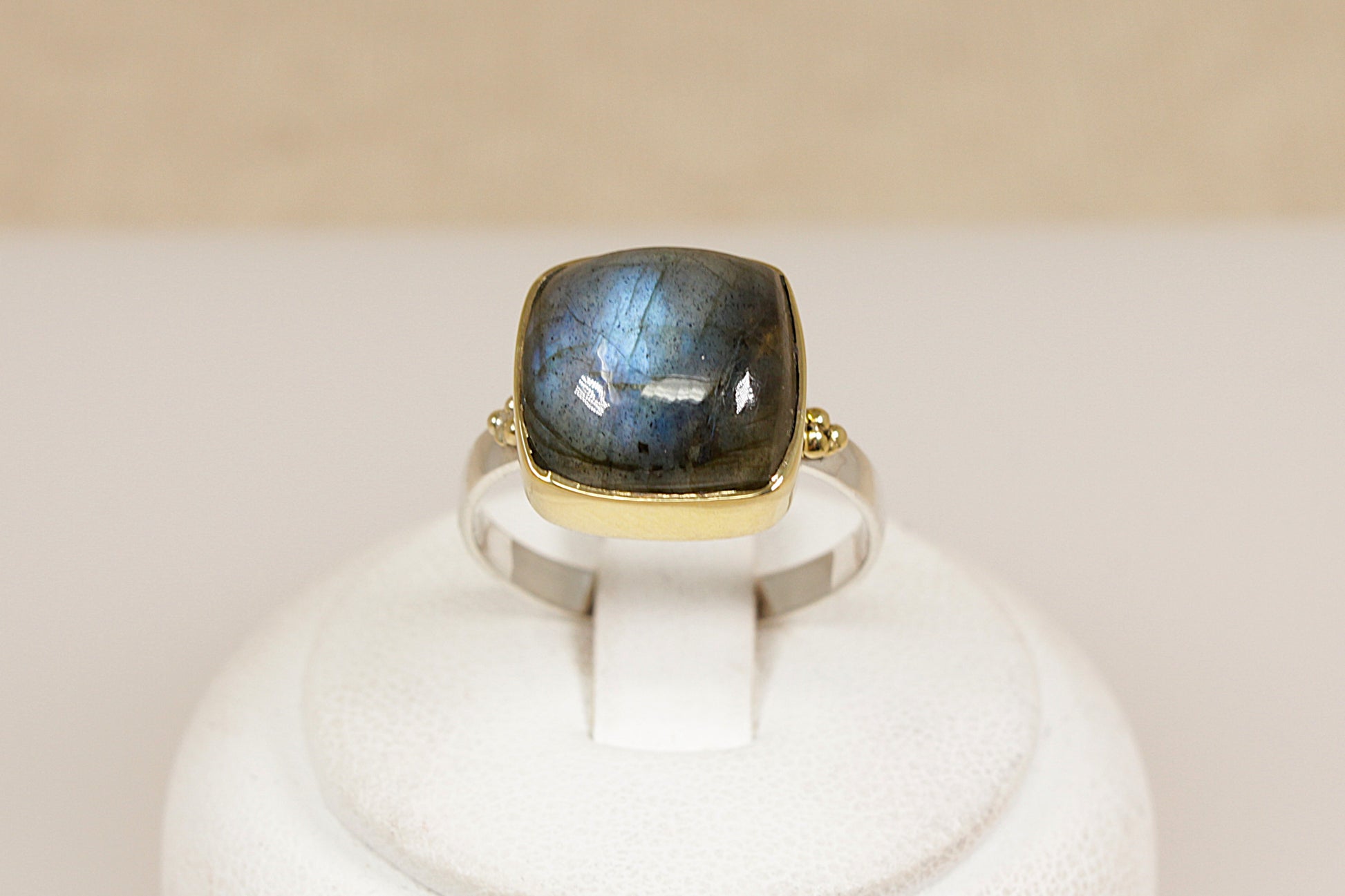 Ring with a labradorite gemstone and gold band on a white stand against a beige background