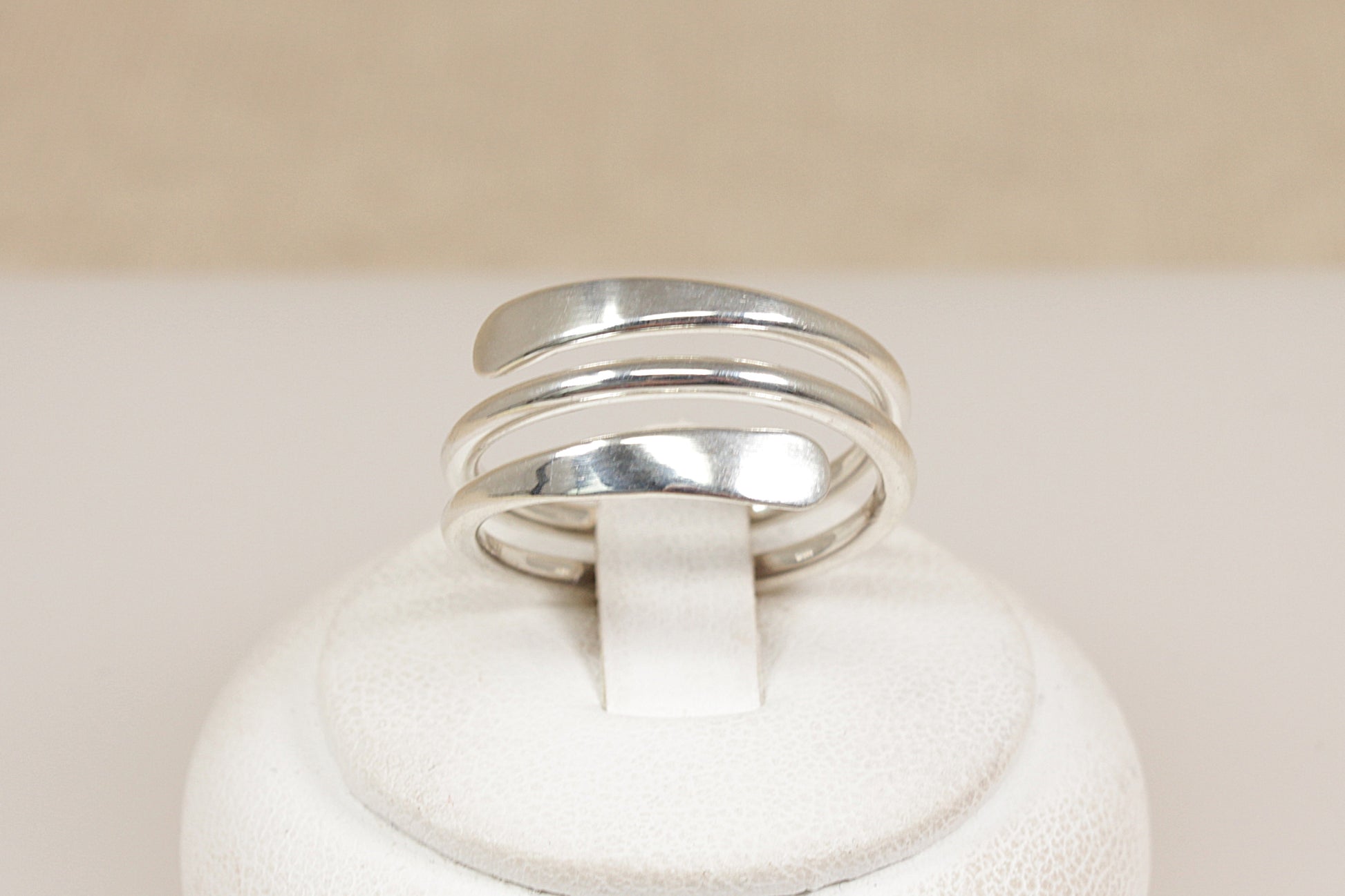 Silver coil ring on a white rind stand  with a beige background
