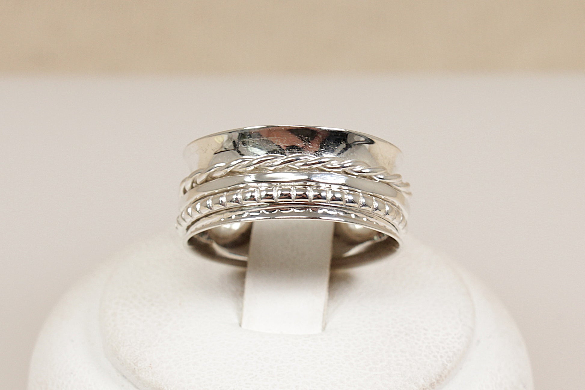 Silver ring with intricate design on a white cushion