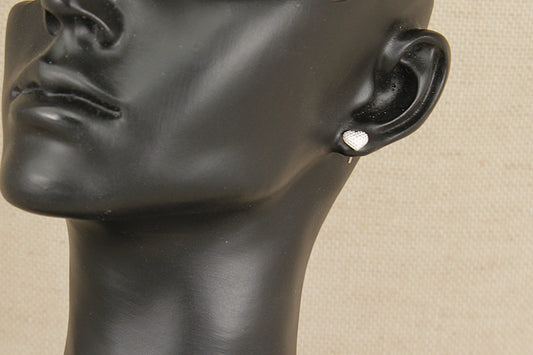 Black mannequin head with a silver heart earring on a beige background