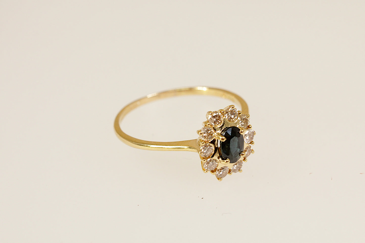 Gold ring with a blue sapphire gemstone and smaller diamonds on a beige background