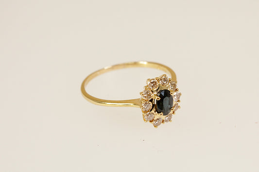 Gold ring with a blue sapphire gemstone and smaller diamonds on a beige background
