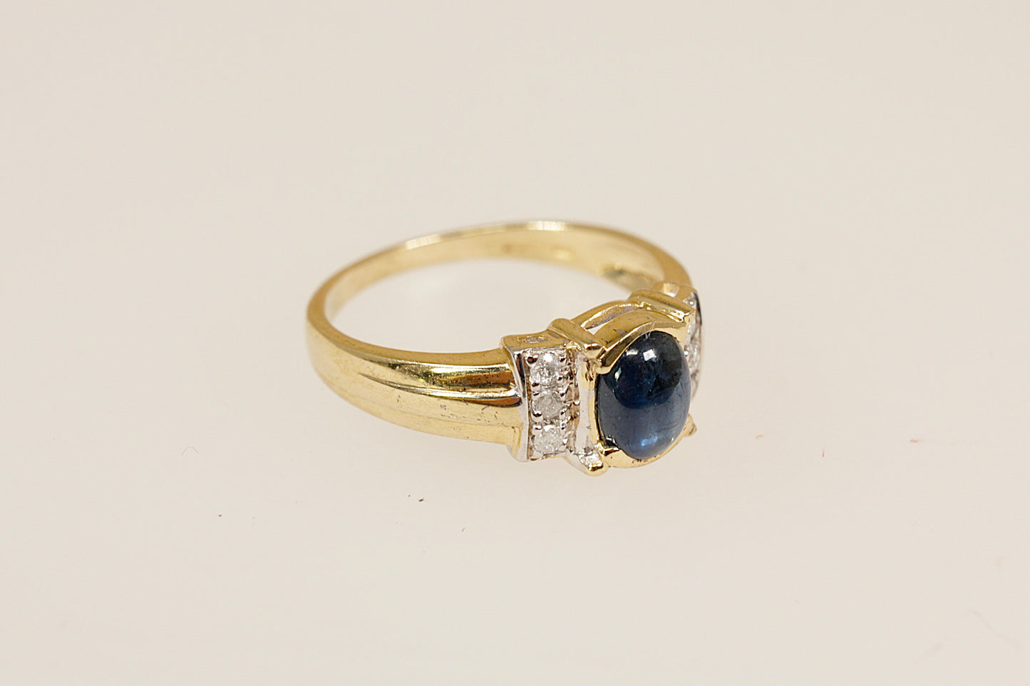 Gold ring with a blue sapphire gemstone and diamond accents on a beige background