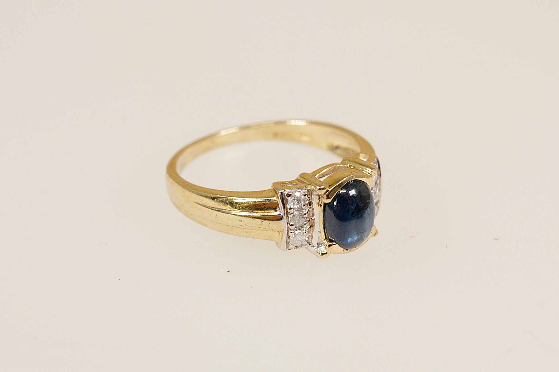 Gold ring with a blue sapphire gemstone and diamond accents on a beige background