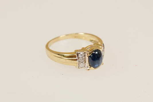 Gold ring with a blue sapphire gemstone and diamond accents on a beige background