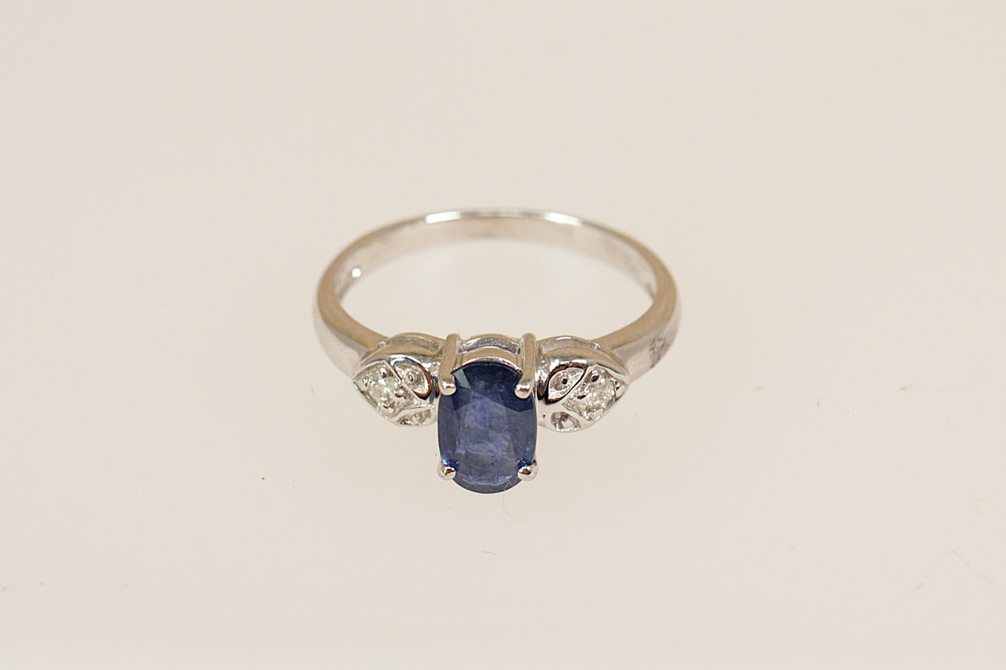 White gold ring with a blue sapphire gemstone and smaller diamonds on a beige background