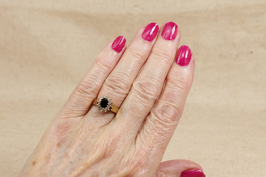 A beautiful and classic 18ct Sapphire and Diamond “Diana” style cluster ring on hand with beige background.