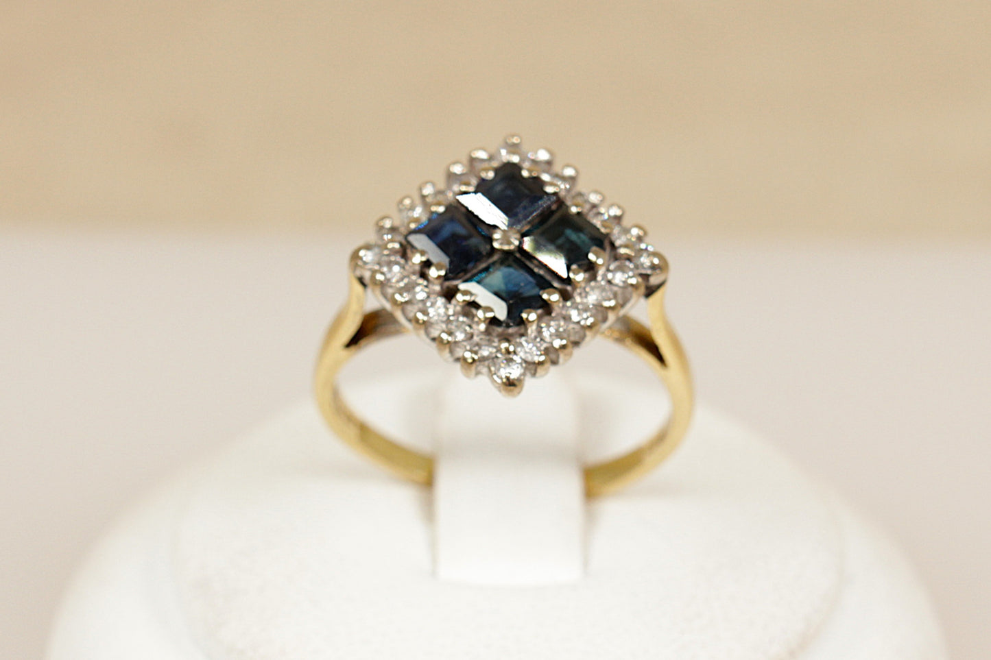 18ct Gold ring with blue sapphire gemstone and diamond accents on a beige background