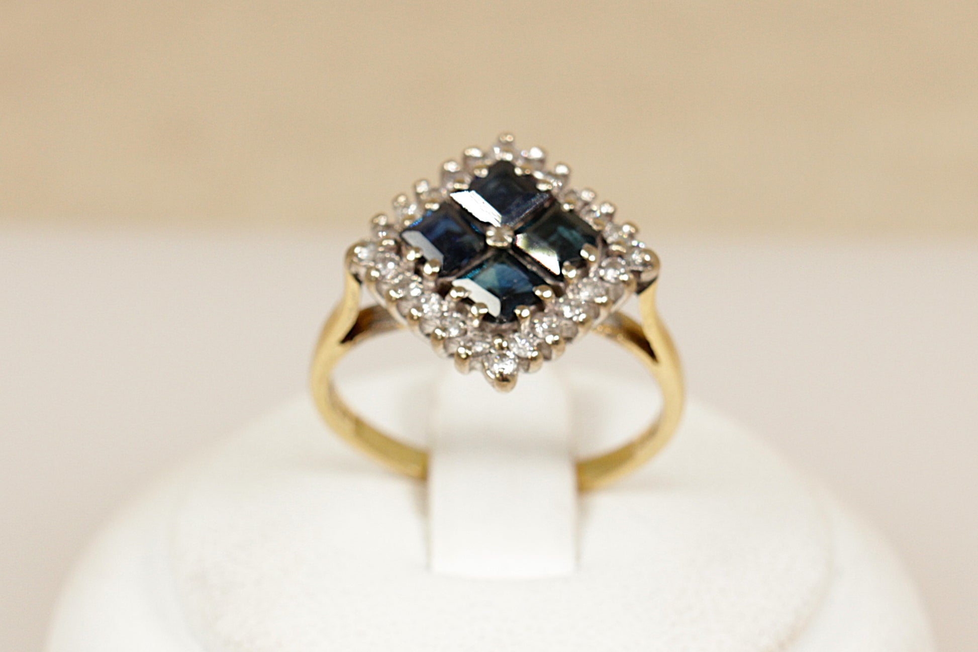 18ct Gold ring with blue sapphire gemstone and diamond accents on a beige background