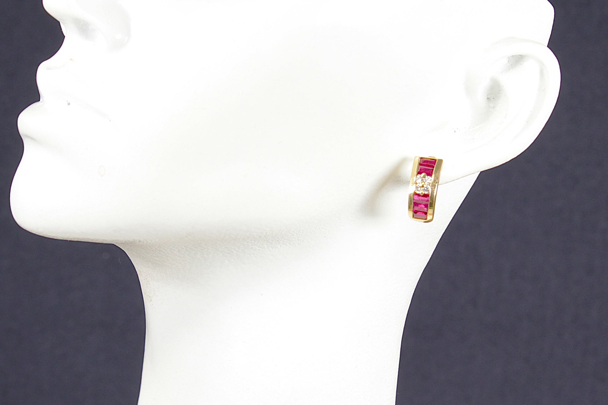 Gold earrings with red ruby gemstones and central diamonds on a mannequin ear