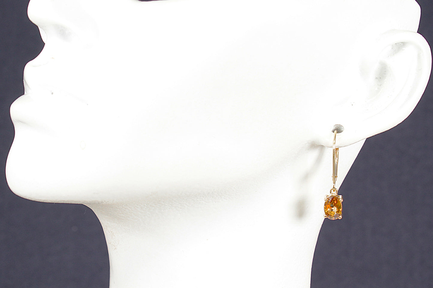 Gold earring with a honey citrine gemstone on a white mannequin head.