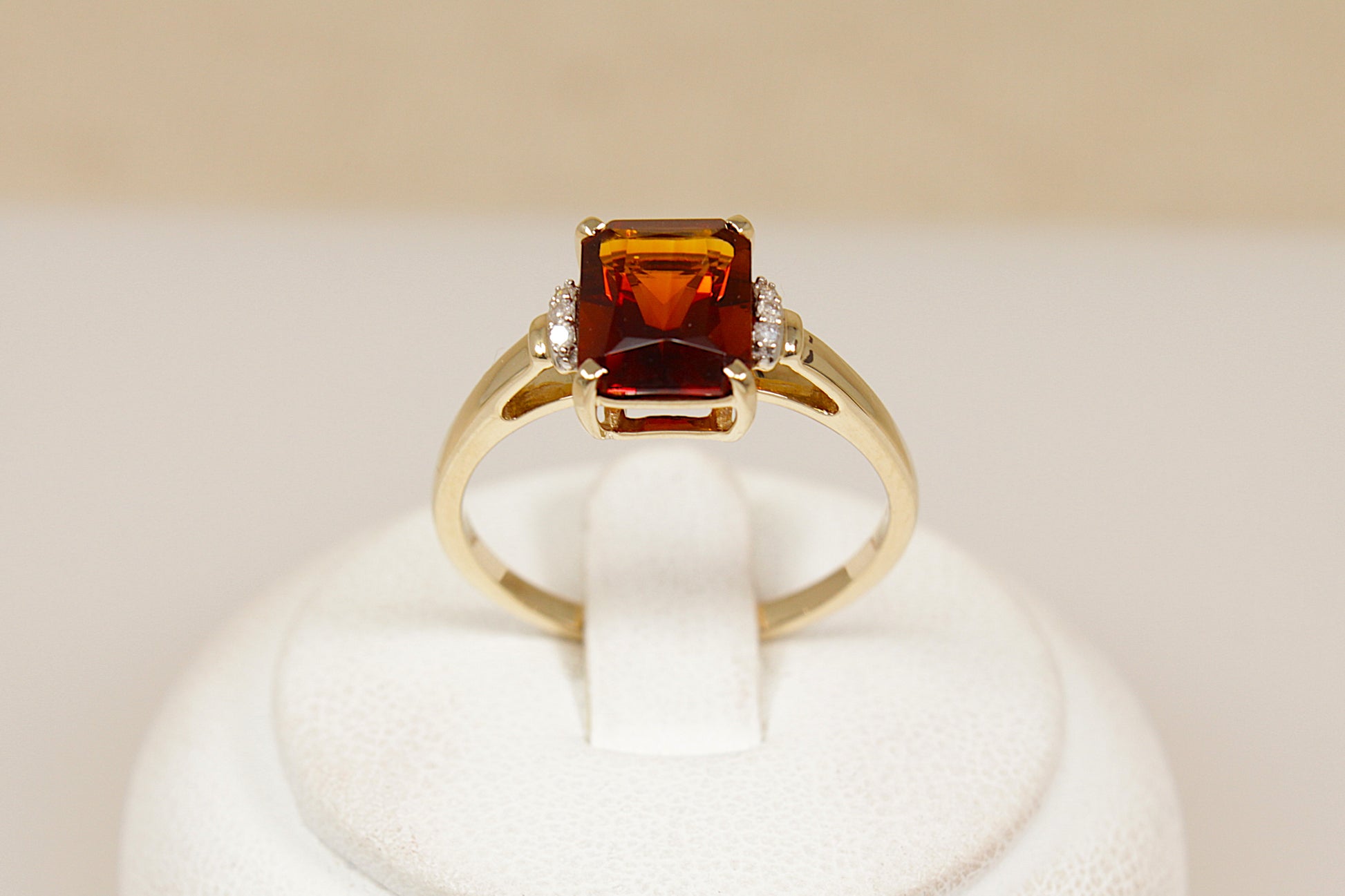 Gold ring with a prominent red almandine garnet gemstone on a white stand against a beige background