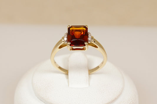 Gold ring with a prominent red almandine garnet gemstone on a white stand against a beige background