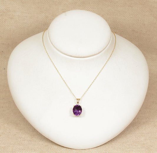 Gold necklace with a purple amethyst pendant on a white stand against a beige background