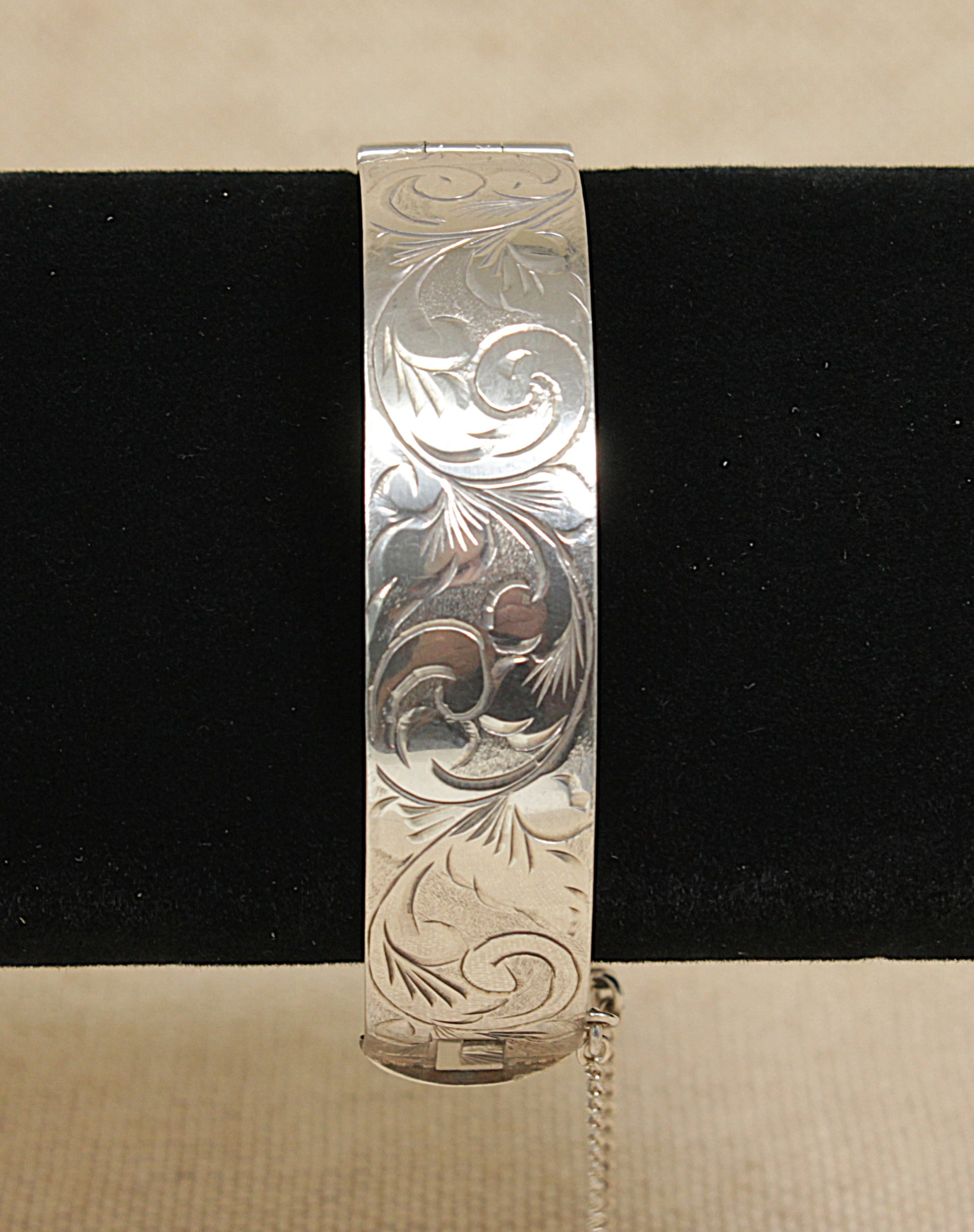 Vintage solid silver bracelet with intricate floral patterns on a black stand against a beige background