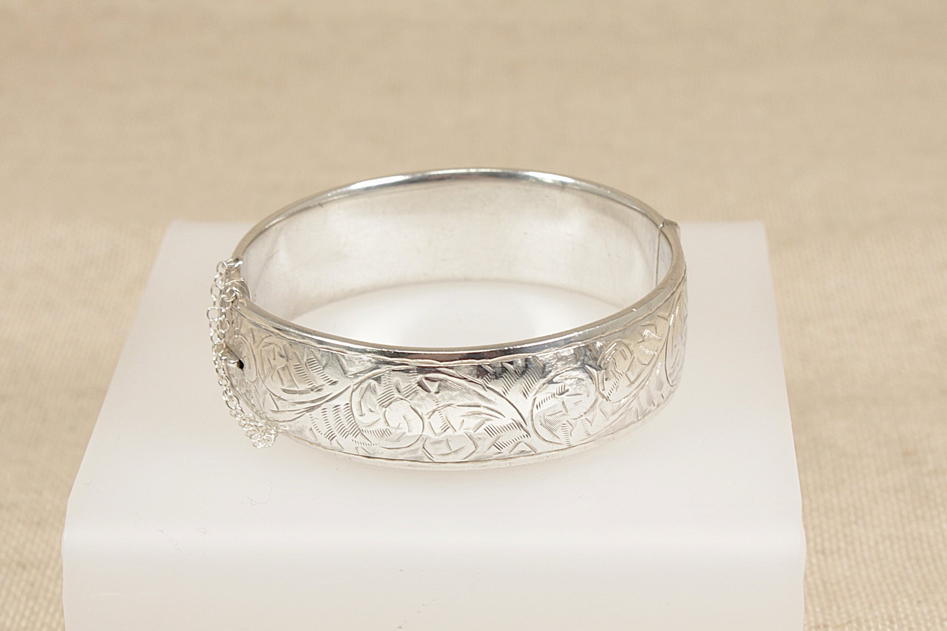 Silver bracelet cuff bangle with intricate designs on a beige background