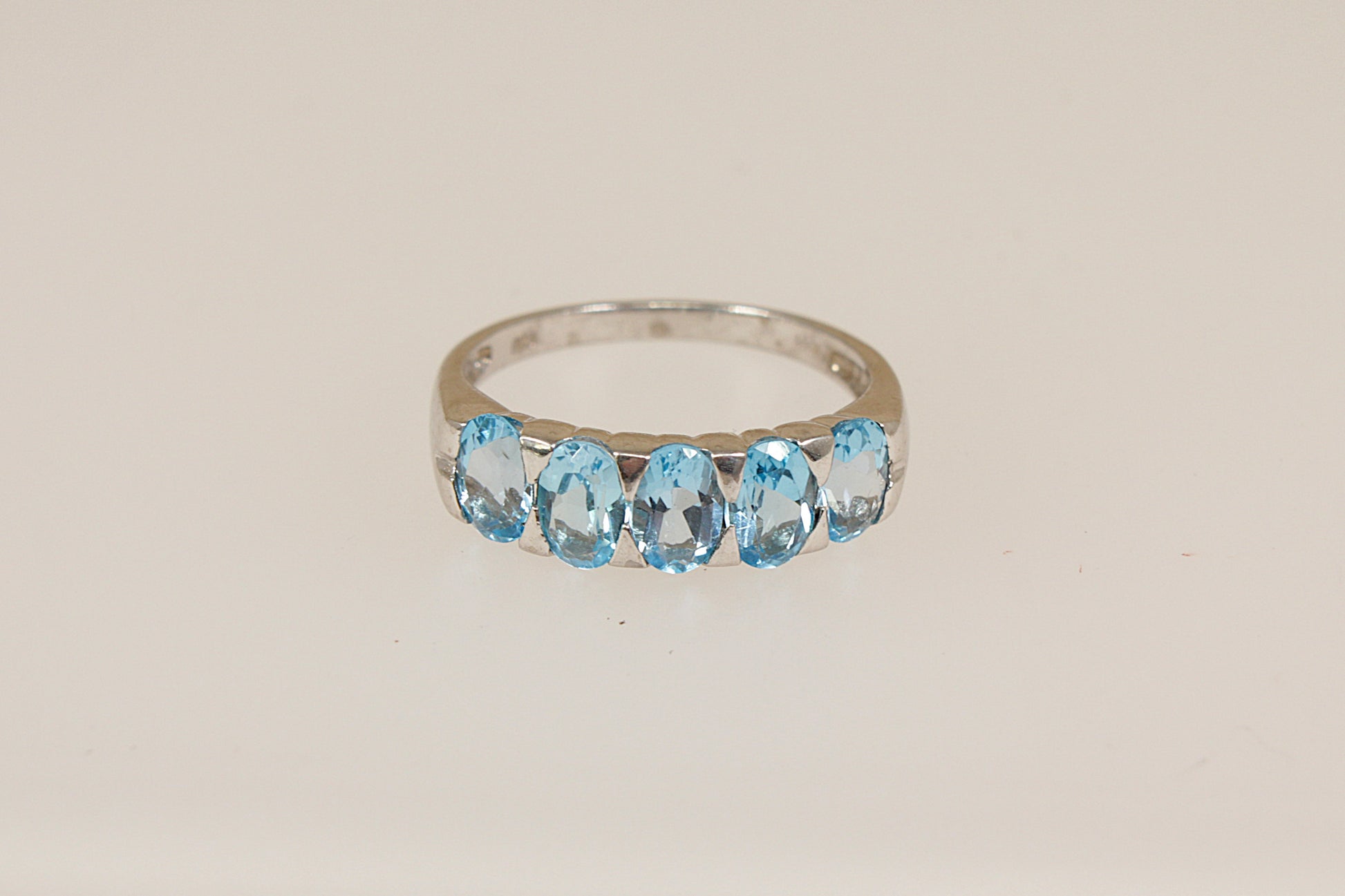 Silver ring with blue topaz gemstones on a beige background
