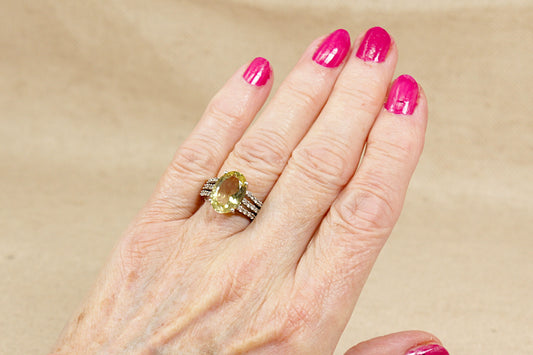 Hand with pink nail polish wearing a lemon citrine gemstone solitaire ring on a beige background