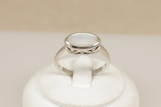 Silver ring with a white mother of pearl shell gemstone on a beige background