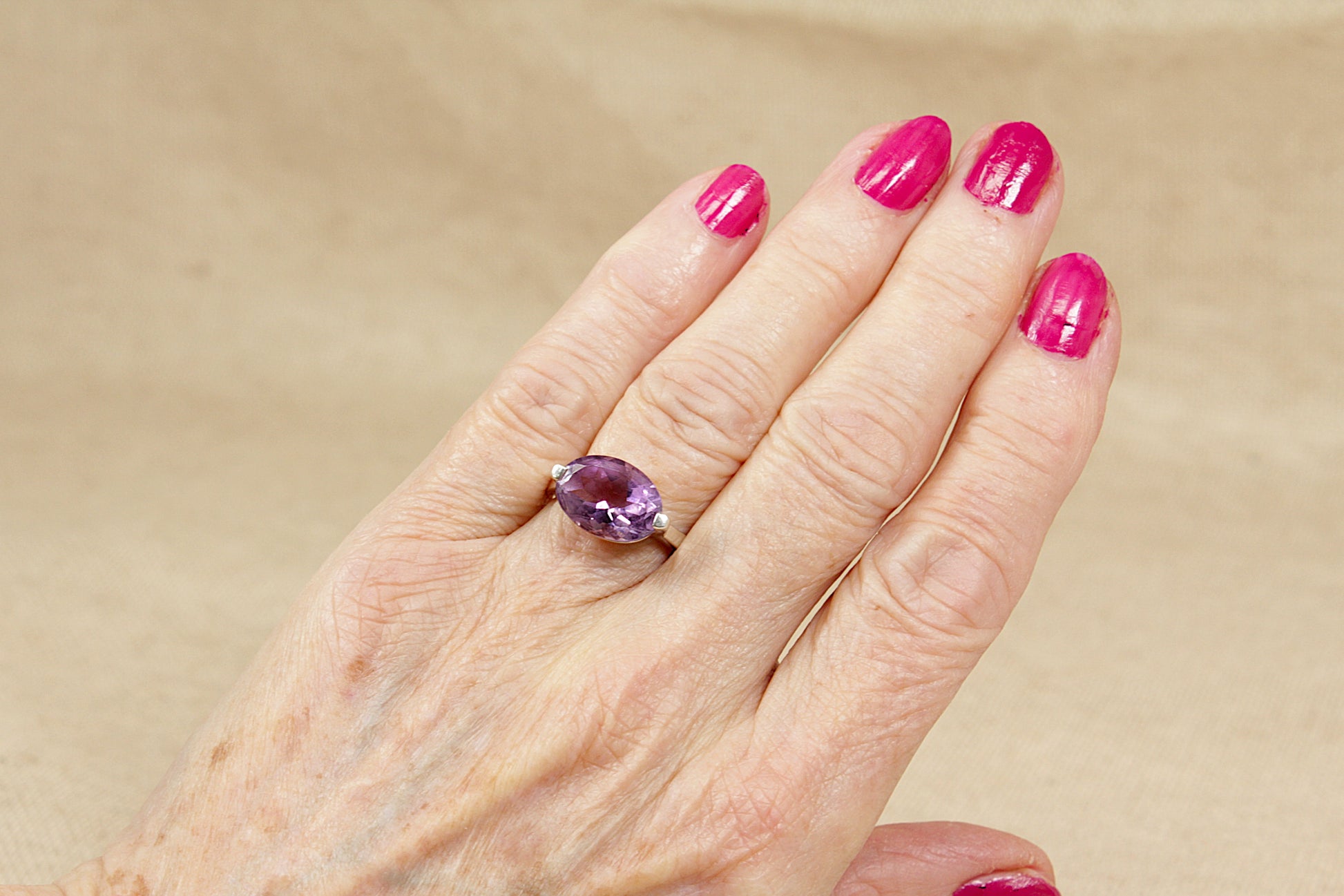 Hand wearing a ring with a purple amethyst gemstone on a beige background