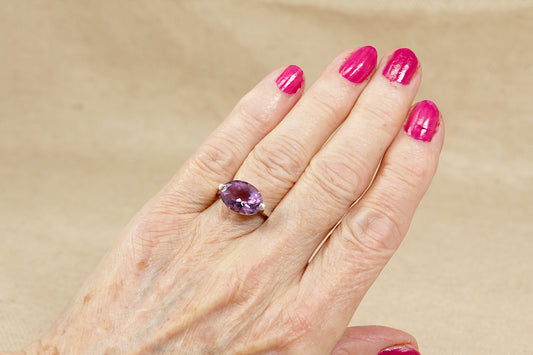 Hand wearing a ring with a purple amethyst gemstone on a beige background