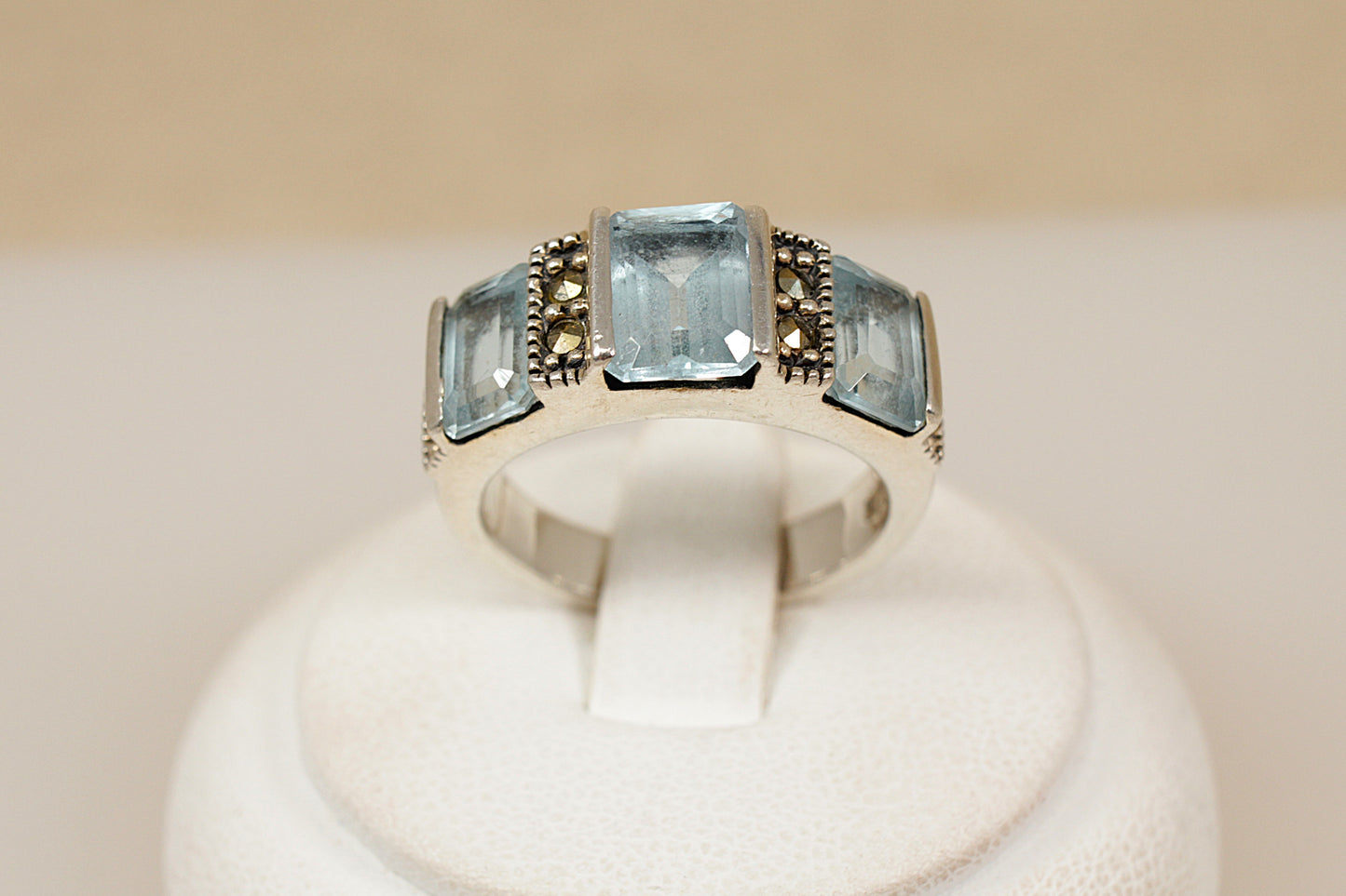 Silver ring with three blue topaz gemstones on a white stand