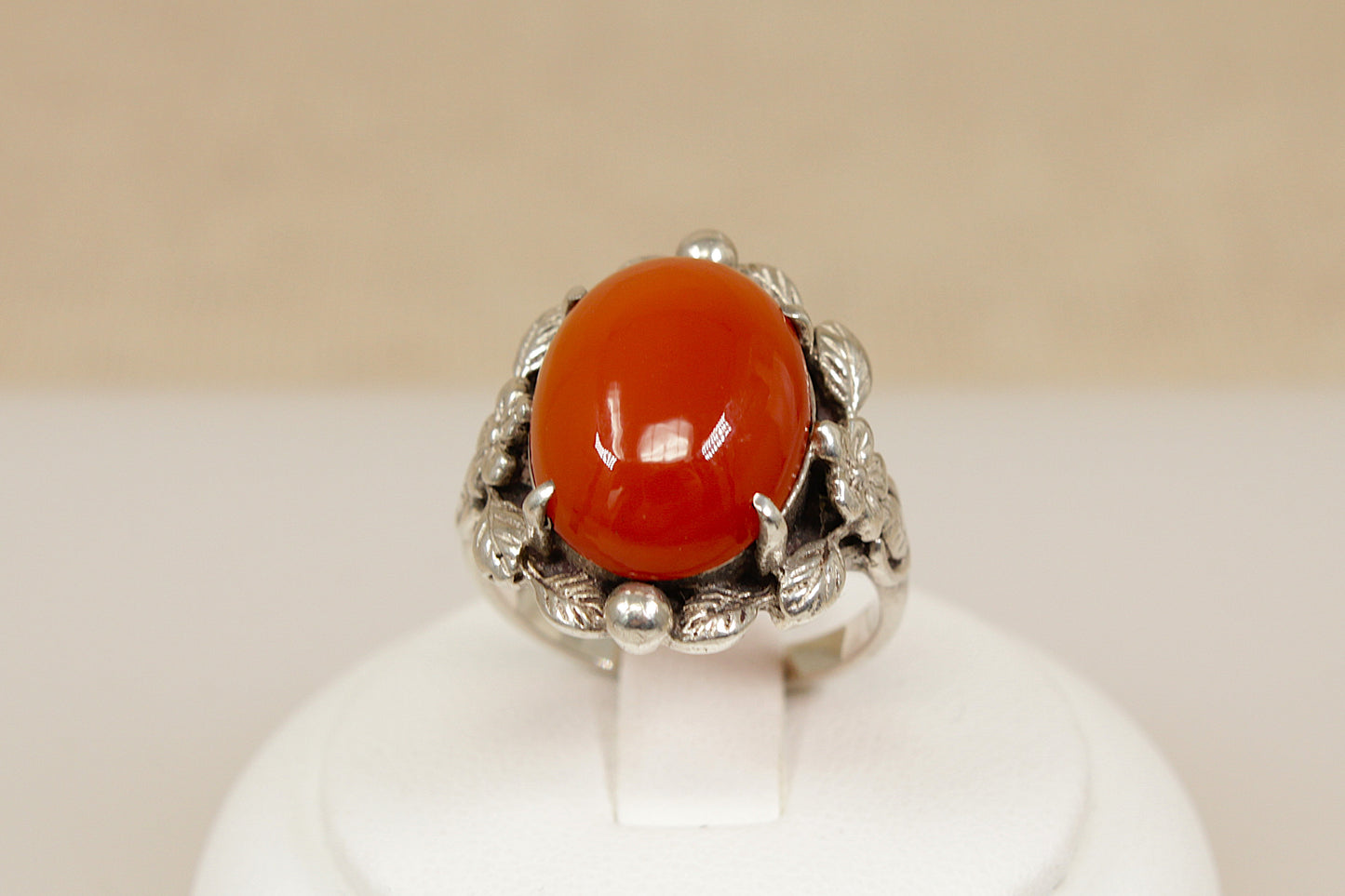 Silver arts and crafts ring with a large red carnelian gemstone on a white stand against a beige background