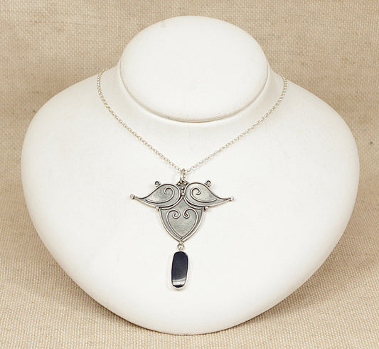 Silver necklace with an opal pendant on a white stand against a beige background