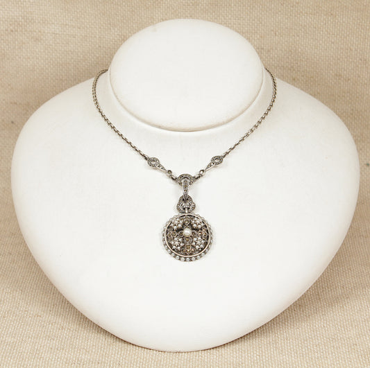 Vintage marcasite necklace with a decorative pearl and seed pearl pendant on a white stand against a beige background