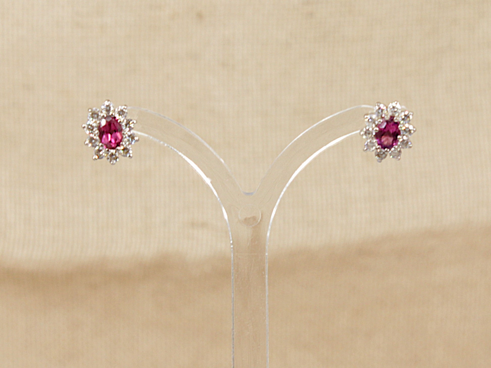 Pair of earrings with red almandine garnet gemstone surrounded by a halo of cz gemstones  on a beige background