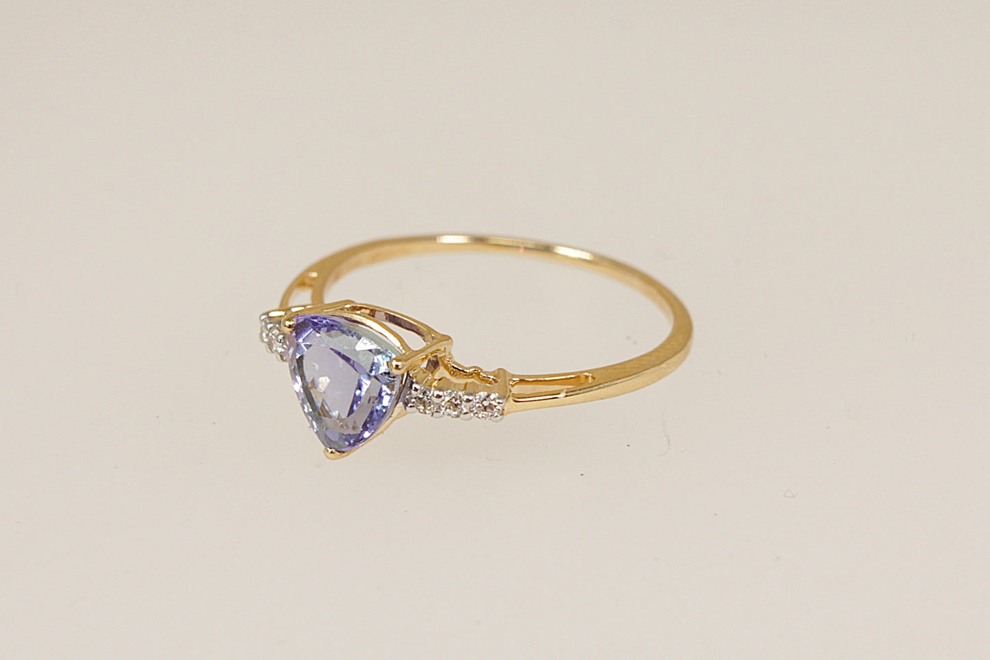 Gold ring with a trillion cut tanzanite  gemstone with diamond accents on each shoulder on a beige background