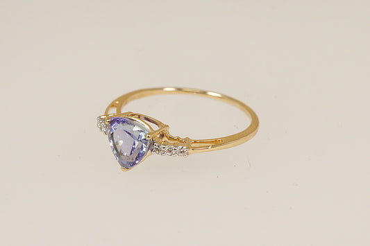 Gold ring with a trillion cut tanzanite  gemstone with diamond accents on each shoulder on a beige background