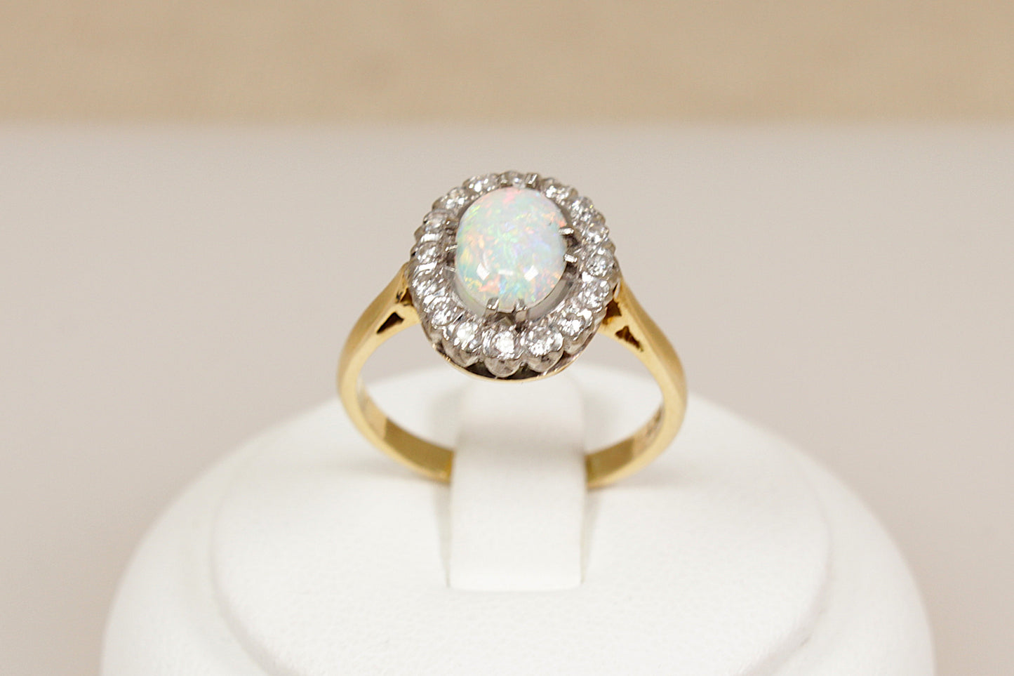 18ct gold ring with central opal gemstone surrounded by diamonds on a white stand