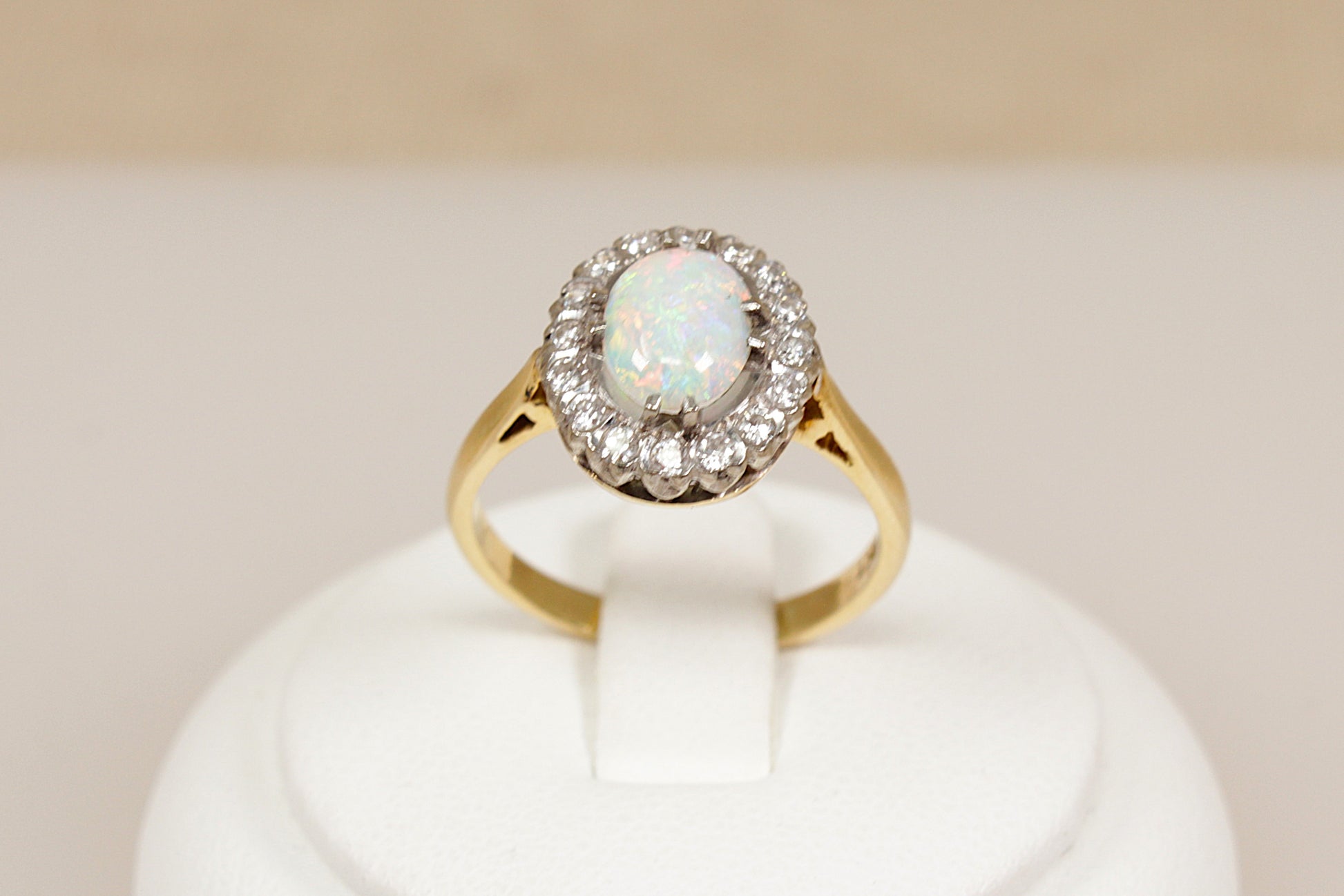 18ct gold ring with central opal gemstone surrounded by diamonds on a white stand
