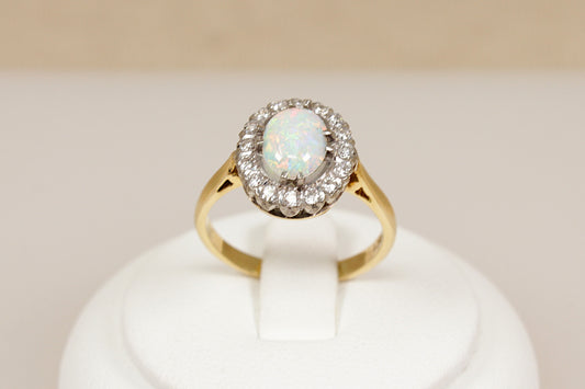 18ct gold ring with central opal gemstone surrounded by diamonds on a white stand