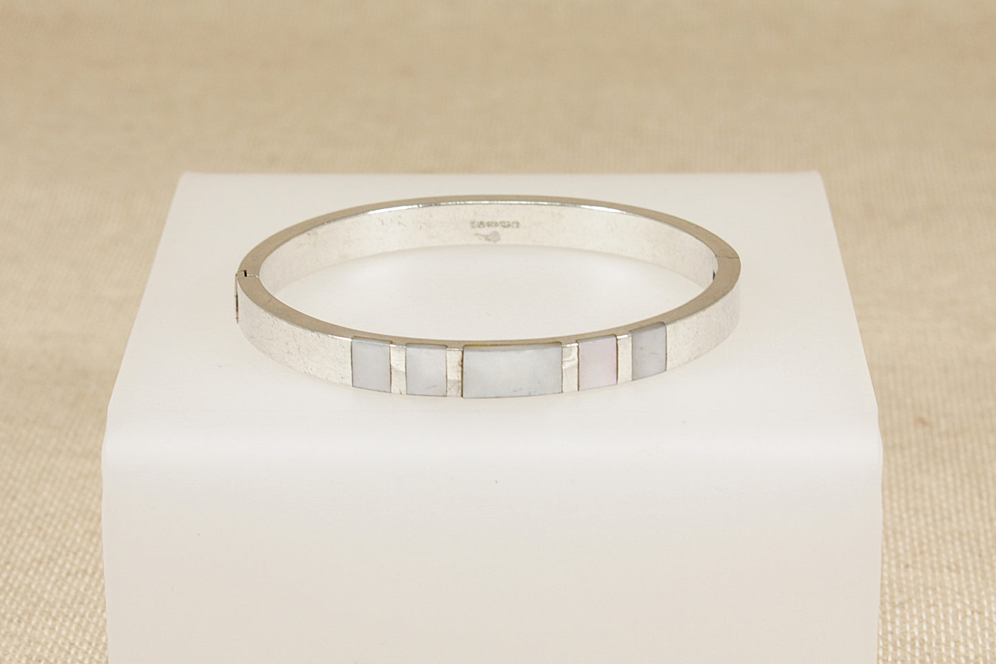 Silver bracelet with a mother of pearl inlay on a white cube against a beige background