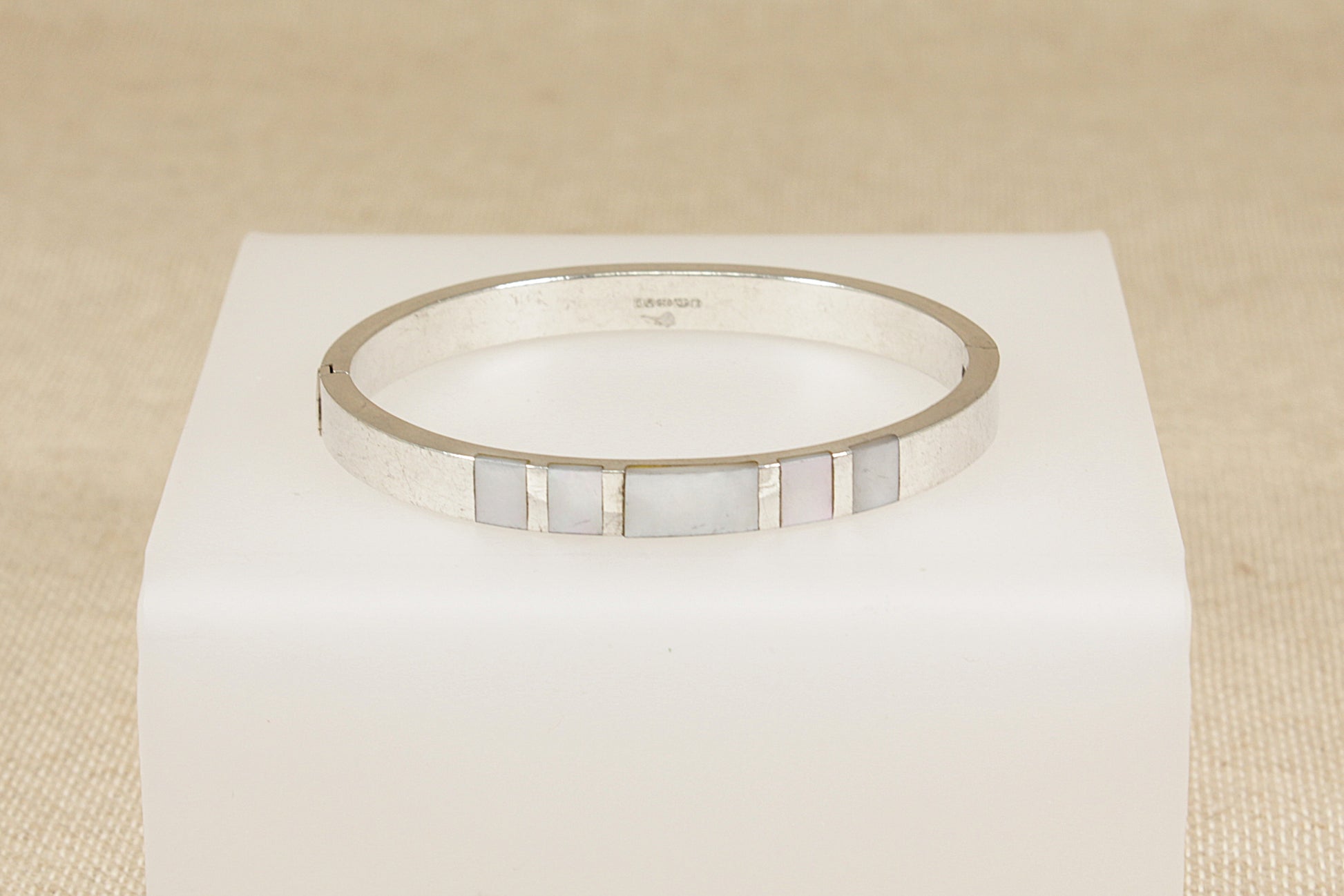 Silver bracelet with a mother of pearl inlay on a white cube against a beige background