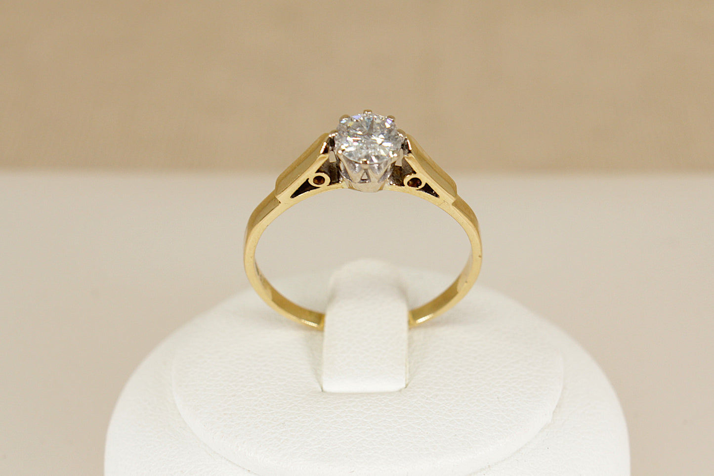 Gold ring with a diamond on a white stand against a beige background