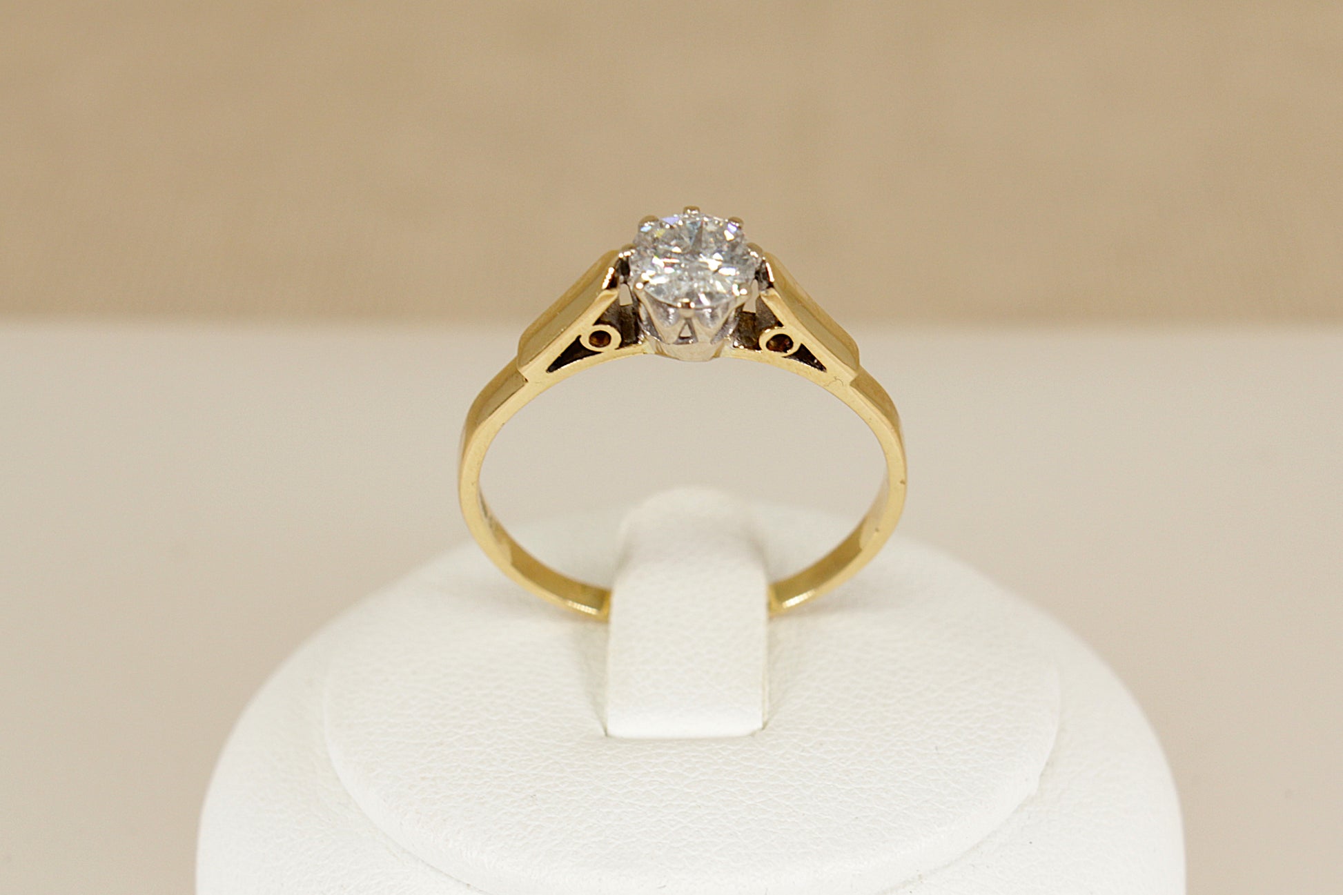 Gold ring with a diamond on a white stand against a beige background