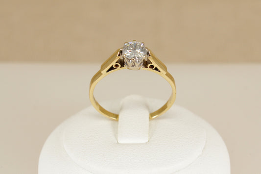 Gold ring with a diamond on a white stand against a beige background