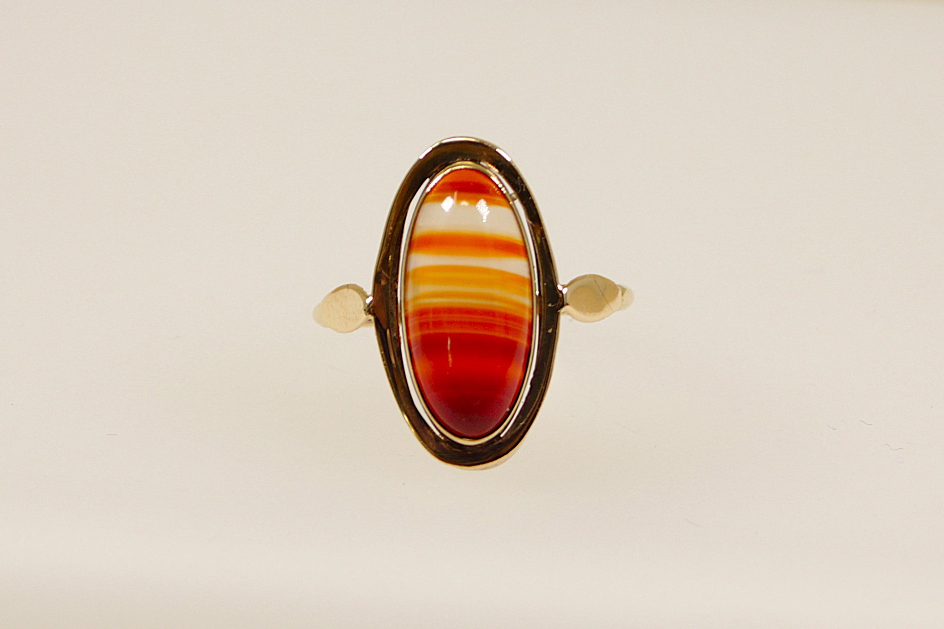 An oval-shaped banded carnelian stone set in a gold ring with the stone displaying reddish-orange hues. The gold band is uncomplicated and elegant, the band is stamped on the outside 333 for 8ct gold, the warm tones of the yellow gold complement the deep colour of the carnelian, creating a harmonious and eye-catching piece. This ring is often associated with vintage or antique styles with a modern twist. UK finger size Q.