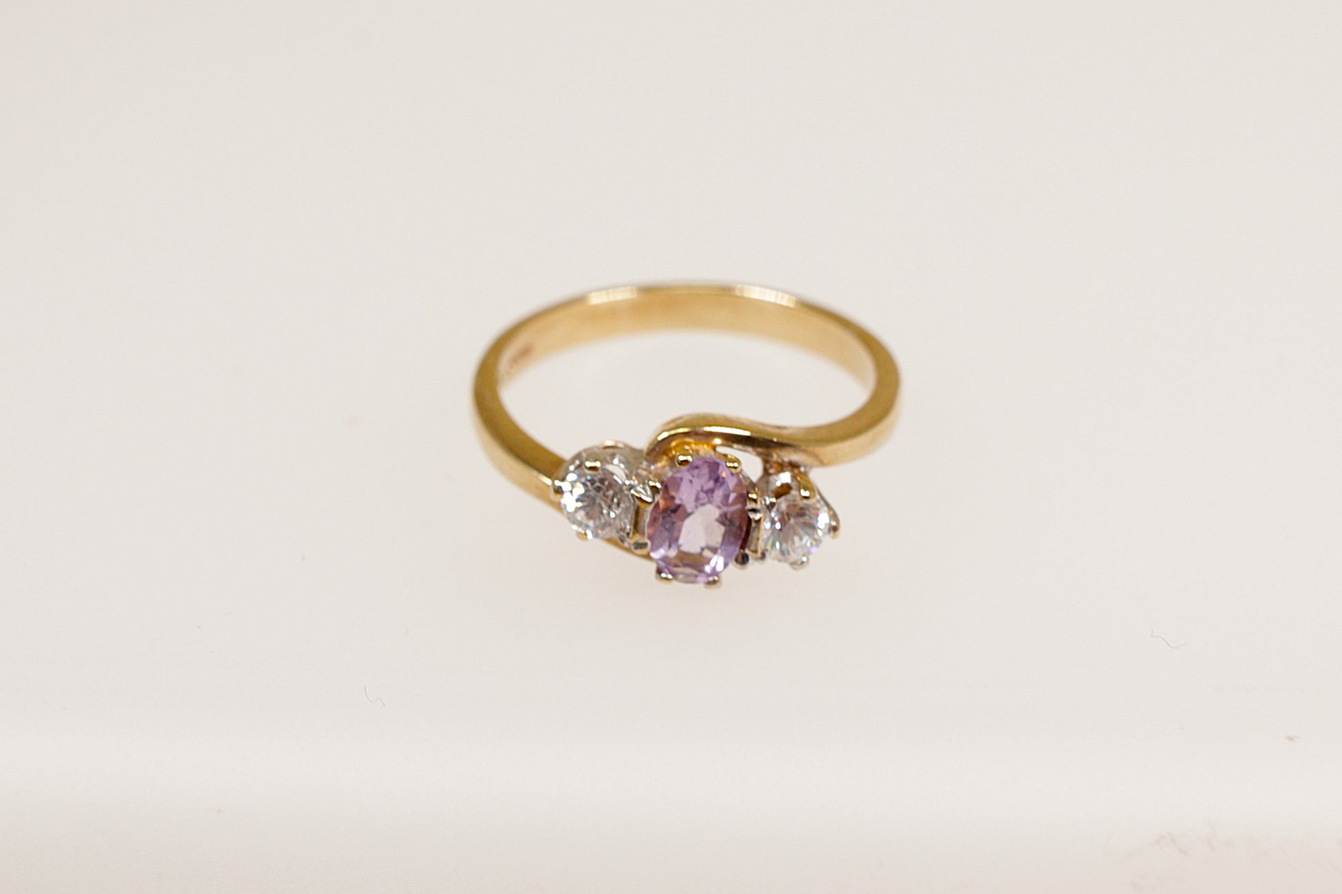 A 9ct gold ring with a central oval amethyst gemstone flanked by two single clear crystal gemstones on each side, Inside the band it has Birmingham hallmarks. UK Finger size N.