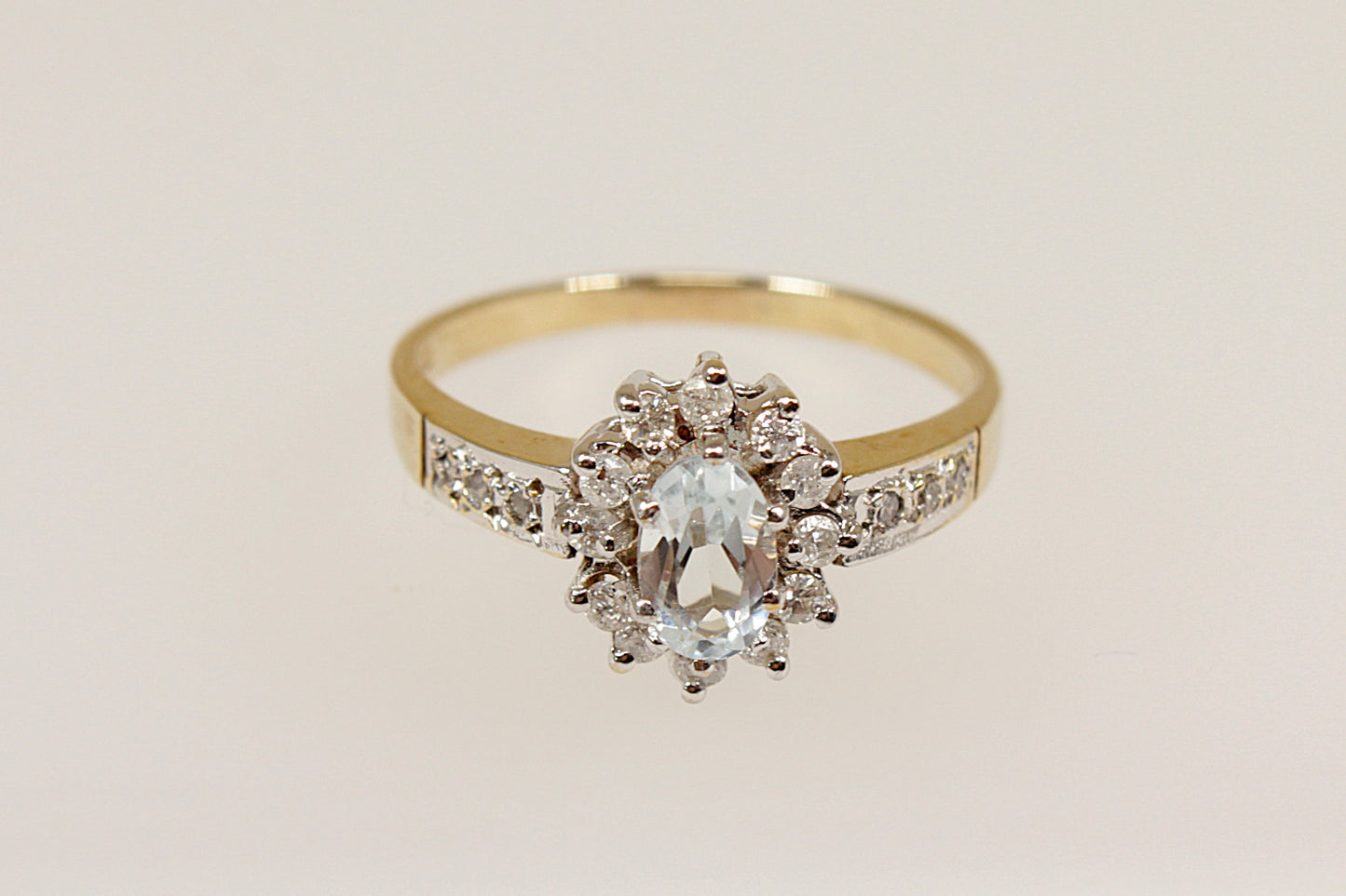 This pretty 9ct Gold ring is an elegant piece of jewellery! It features an oval pale Aquamarine at it’s centre, surrounded by 12 diamonds in a claw setting, with additional Diamonds on each shoulder, UK finger size M.