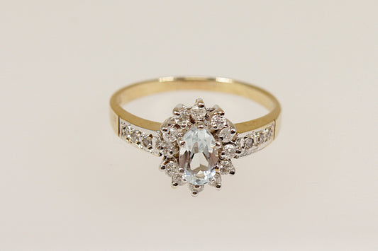 This pretty 9ct Gold ring is an elegant piece of jewellery! It features an oval pale Aquamarine at it’s centre, surrounded by 12 diamonds in a claw setting, with additional Diamonds on each shoulder, UK finger size M.