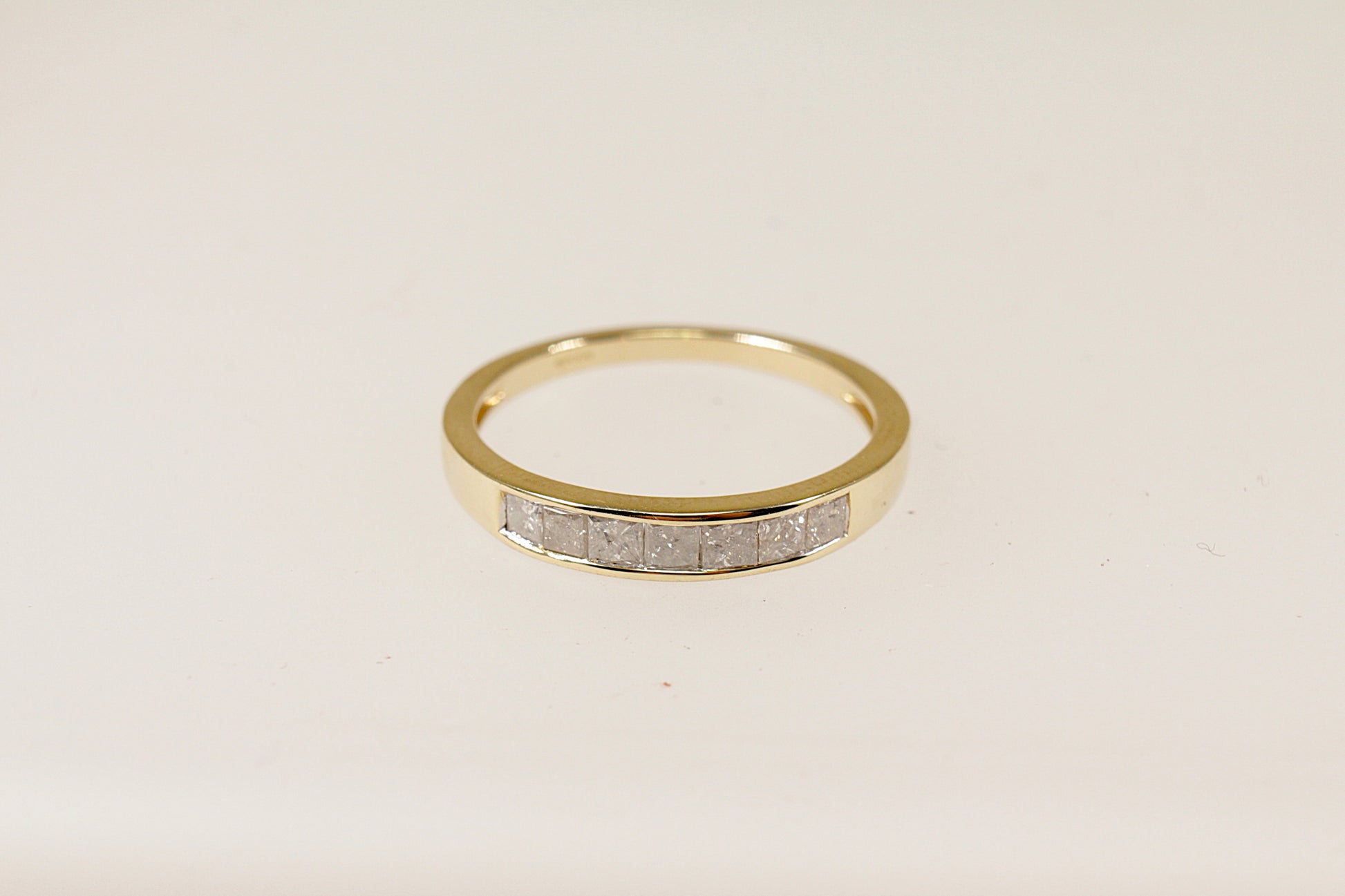A 9ct gold band ring with channel-set princess cut diamonds around the middle section, The ring is in excellent condition and inside the band it has Birmingham hallmarks for 9ct Gold. UK Finger size O