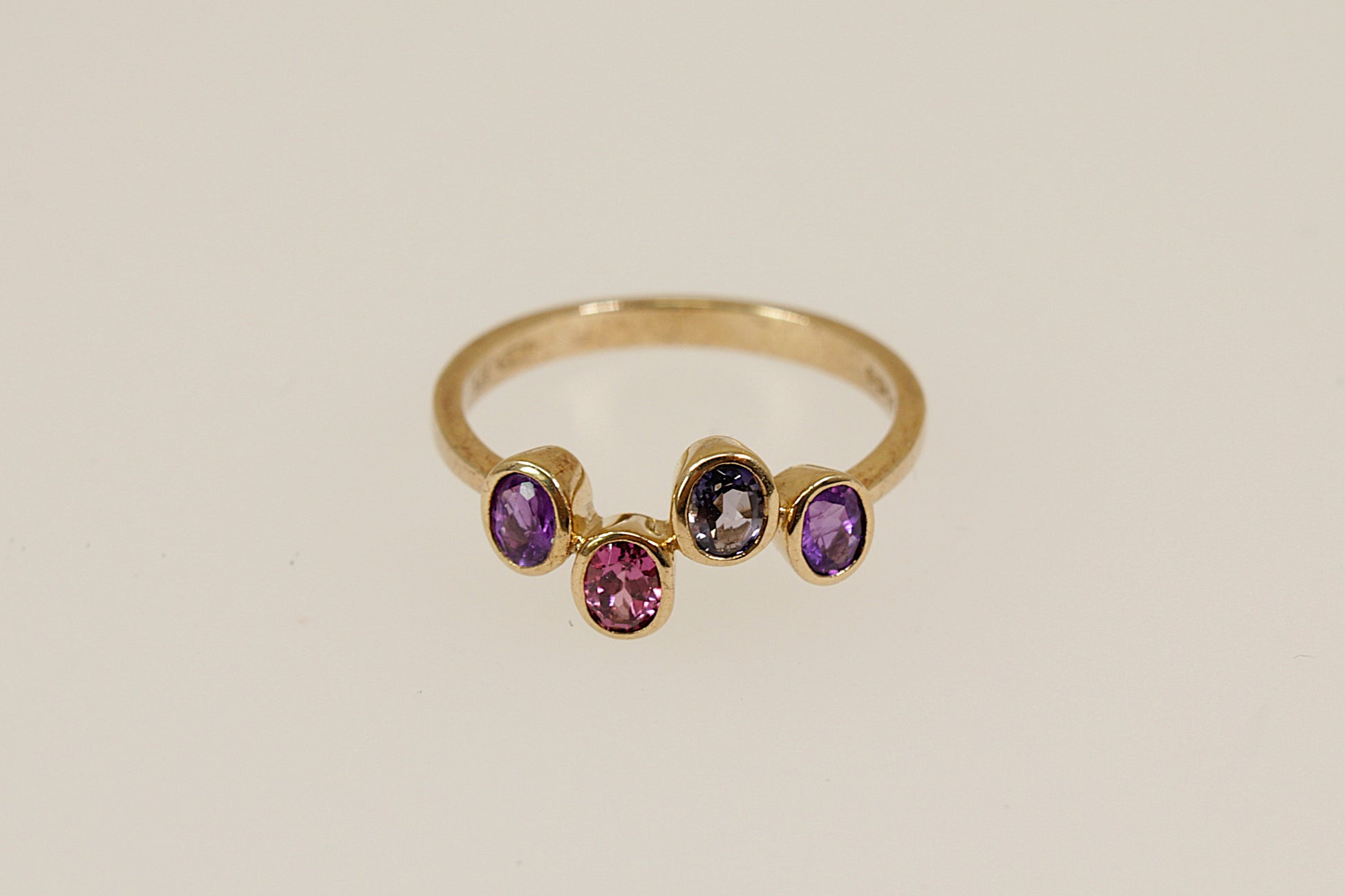 Gold ring with four colored gemstones on a beige background