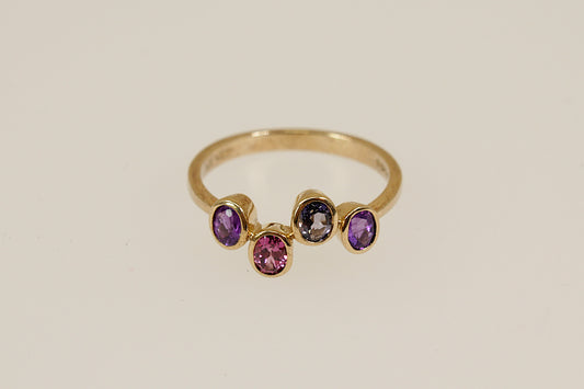 Gold ring with four colored gemstones on a beige background