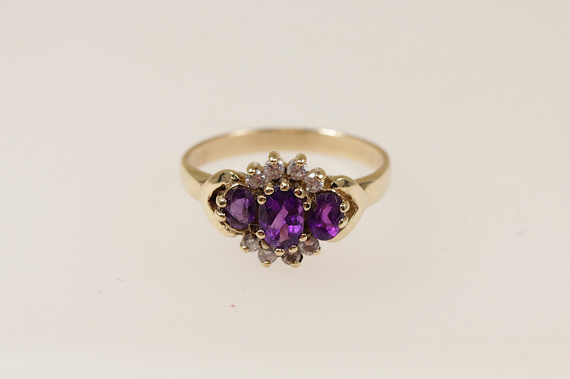 A 9ct gold ring with a floral-inspired design, featuring a central oval amethyst and surrounded by smaller amethysts and cubic zirconia gemstones. UK Finger size O.