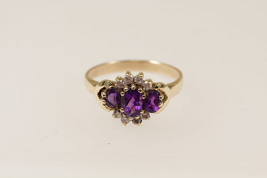 A 9ct gold ring with a floral-inspired design, featuring a central oval amethyst and surrounded by smaller amethysts and cubic zirconia gemstones. UK Finger size O.